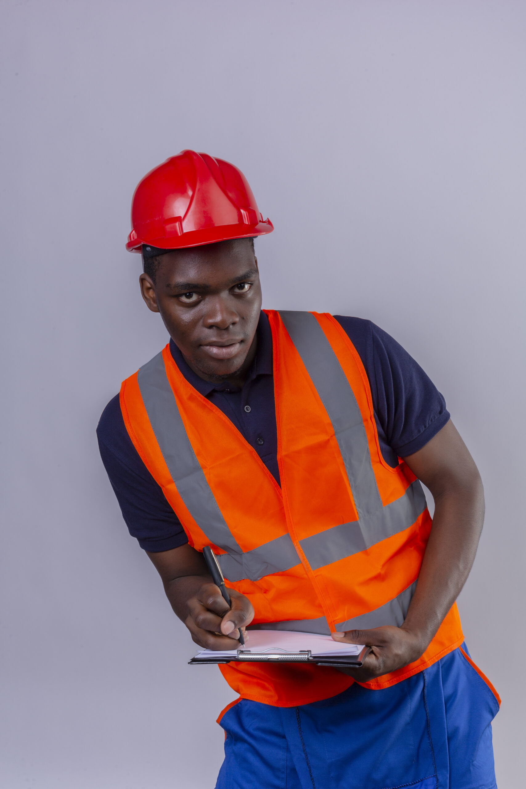 young african american builder man wearing construction vest and safety helmet holding clipboard writing something looking at camera with confident smile standing over white background
